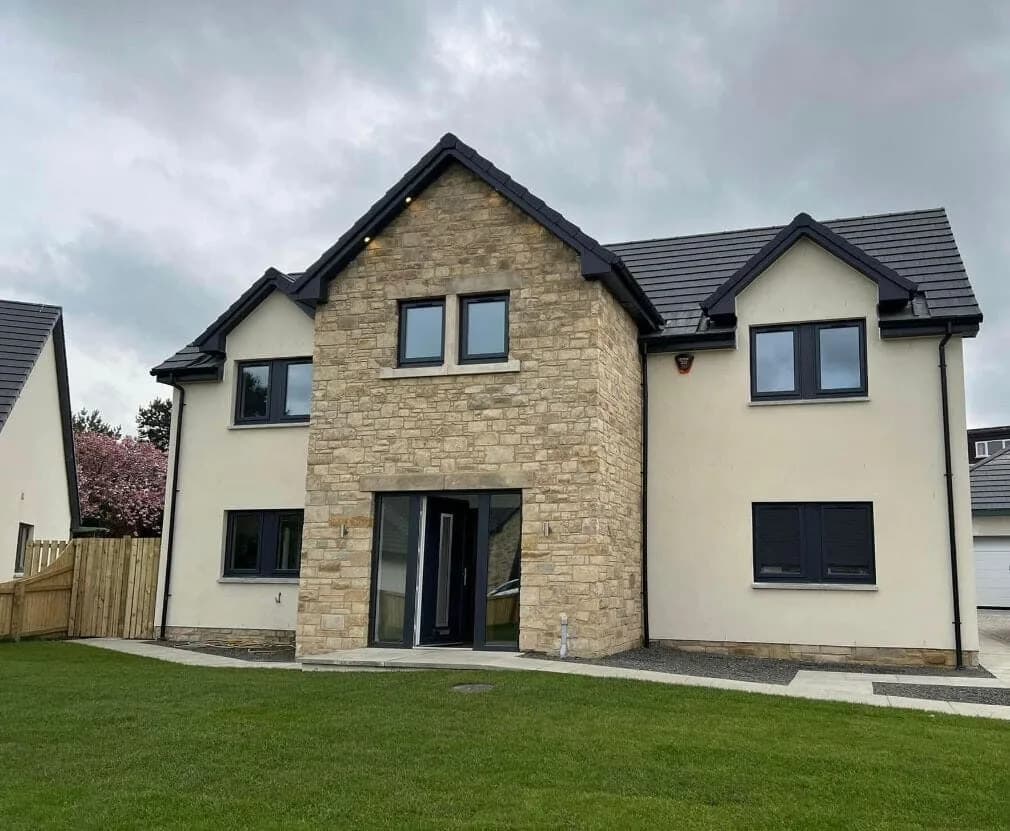 A newly built detached two-storey house with a stone-clad entrance gable, cream render, and dark grey windows.