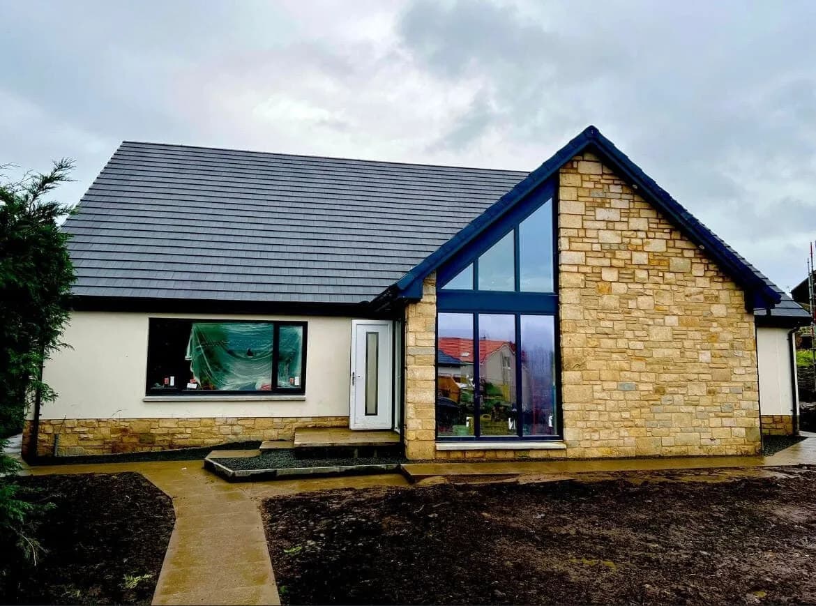 A newly built bungalow with a slate-grey roof, stone and render walls, and a full-height glazed gable.