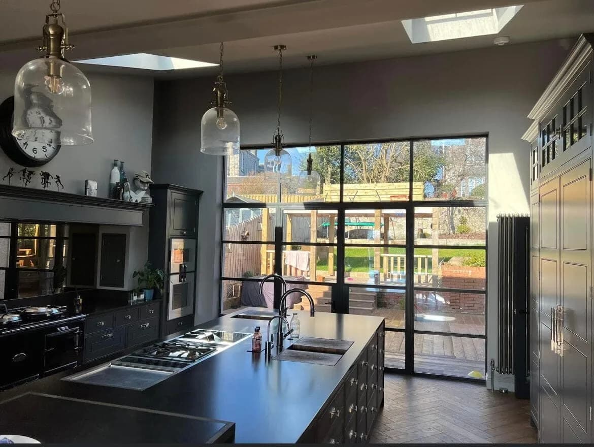 A remodelled open-plan kitchen with dark cabinetry, a large island, pendant lights, roof lights, and glazed doors onto the garden.
